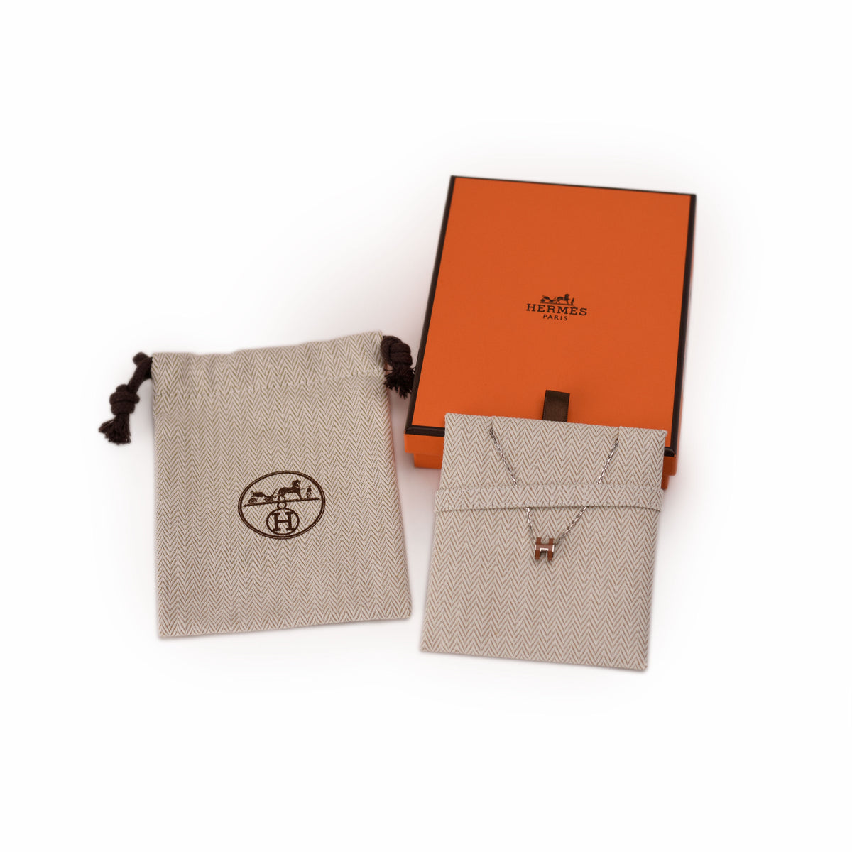 Hermès silver necklace with red H pendant, orange box, and beige pouches. curated Pre-loved Luxury by Myluxe in Helsinki.