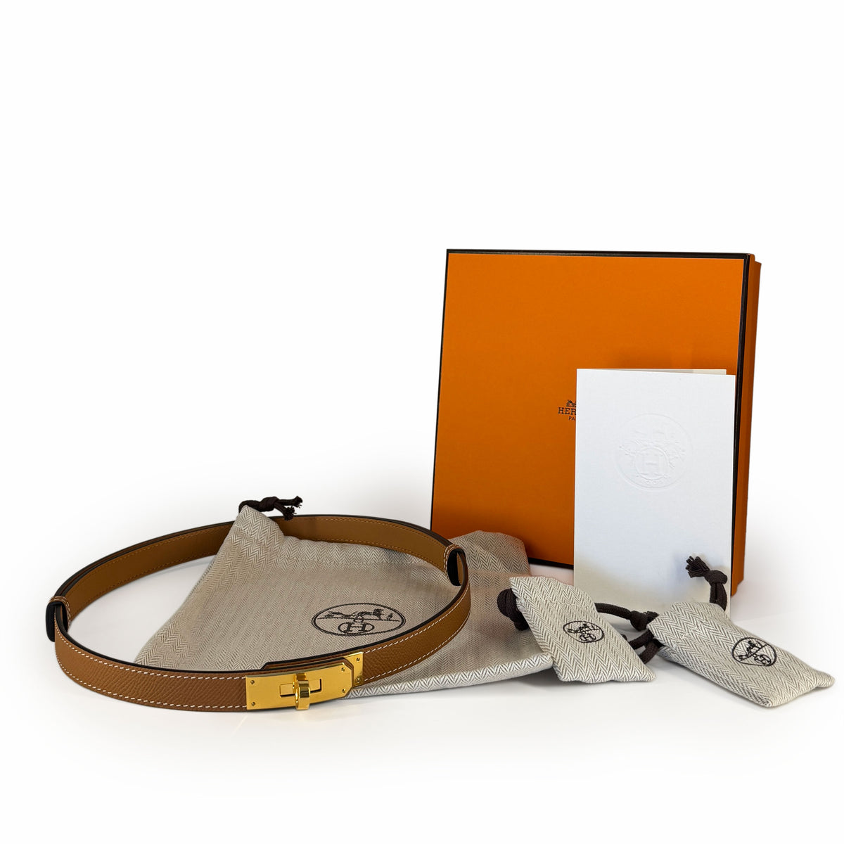 Tan leather belt with gold-tone buckle and Hermès dust bags, curated Pre-loved Luxury by Myluxe in Helsinki.
