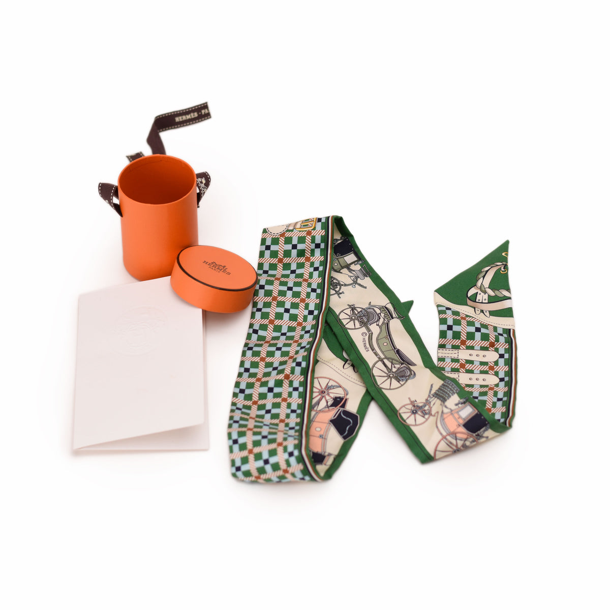 Hermès silk scarf with green equestrian print and orange cylindrical box. curated Pre-loved Luxury by Myluxe in Helsinki.