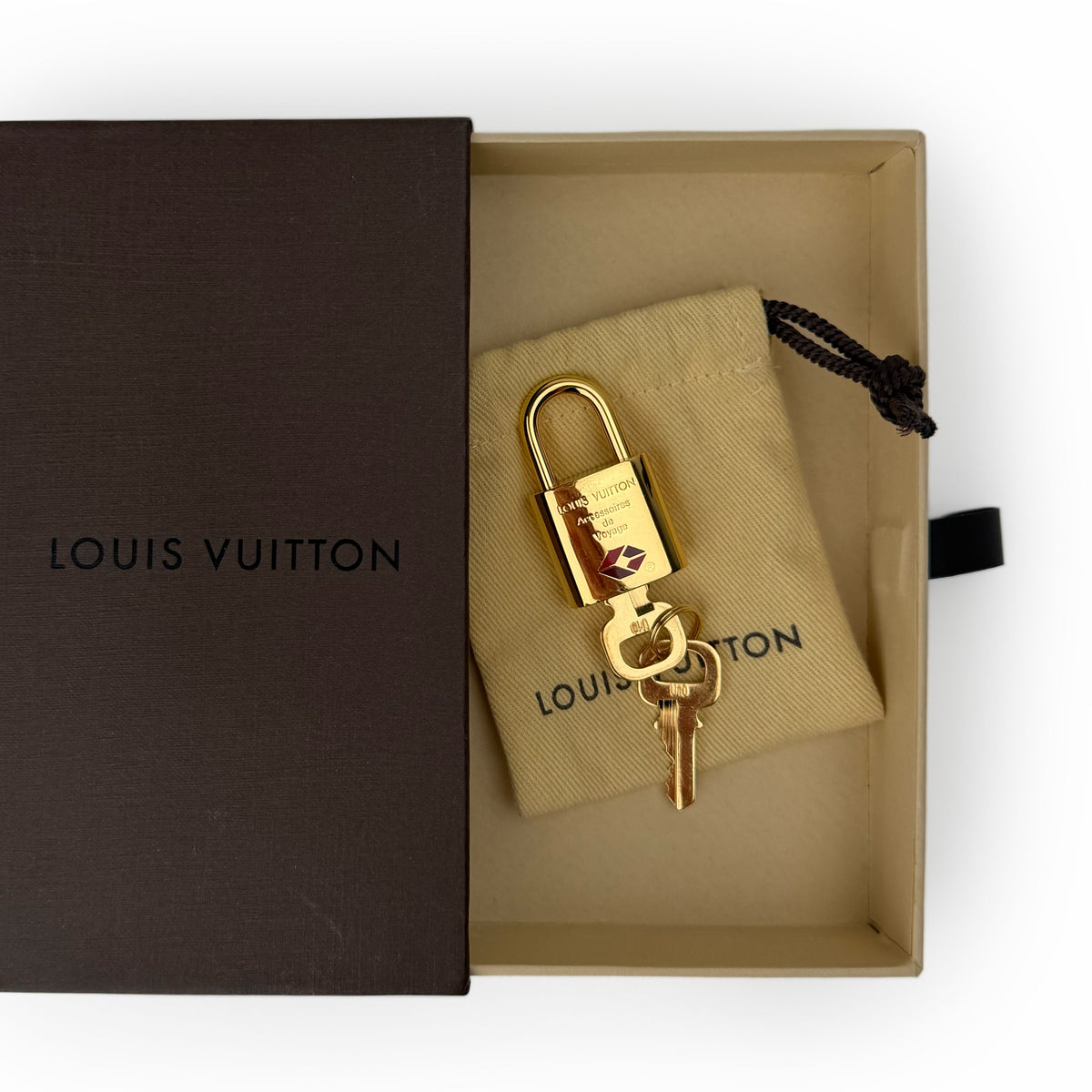 Gold-tone Louis Vuitton padlock and key in a beige pouch and brown box. curated Pre-loved Luxury by Myluxe in Helsinki.