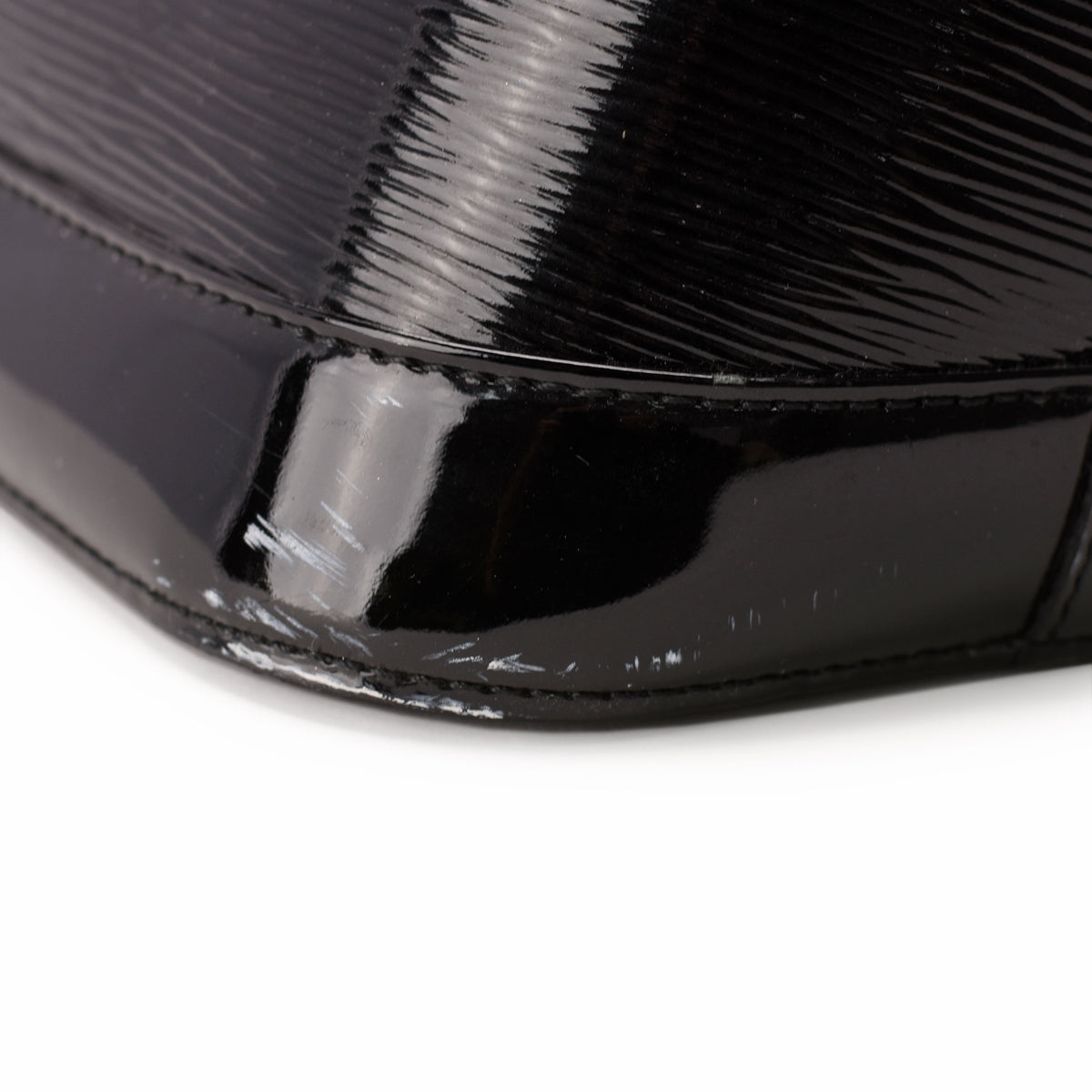 Close-up of a black patent leather handbag corner with minor surface scuffs, curated Pre-loved Luxury by Myluxe in Helsinki.