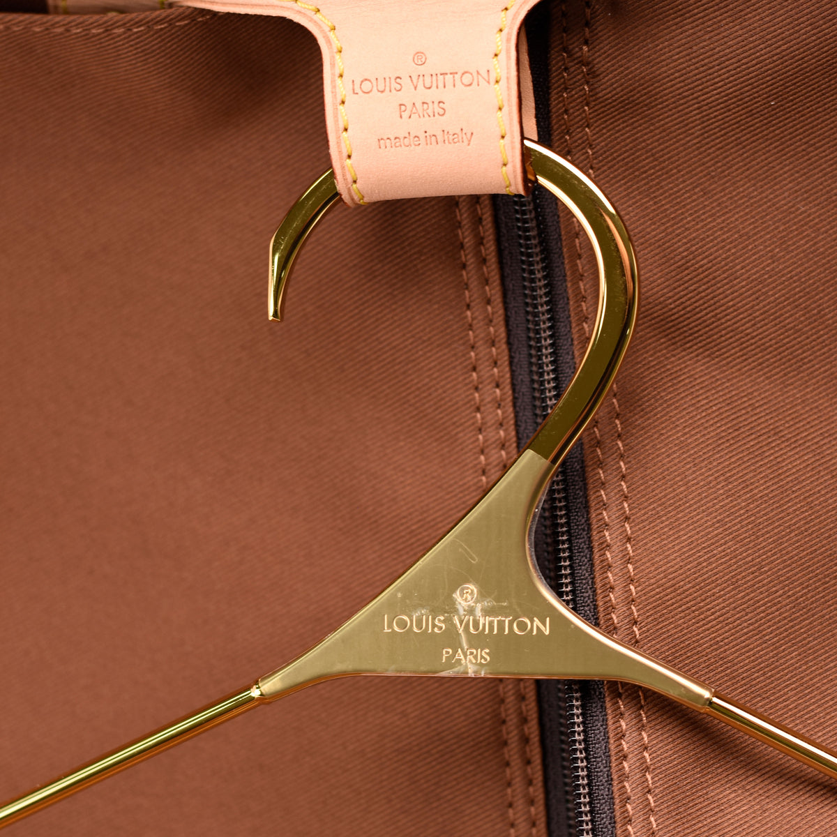 Gold Louis Vuitton hanger on a brown fabric garment, curated Pre-loved Luxury by Myluxe in Helsinki.
