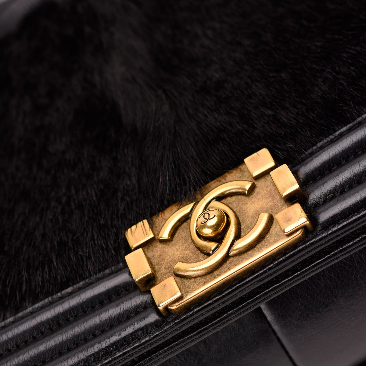 Close-up of a gold Chanel interlocking CC logo on a black fur and leather handbag, curated Pre-loved Luxury by Myluxe in Helsinki.