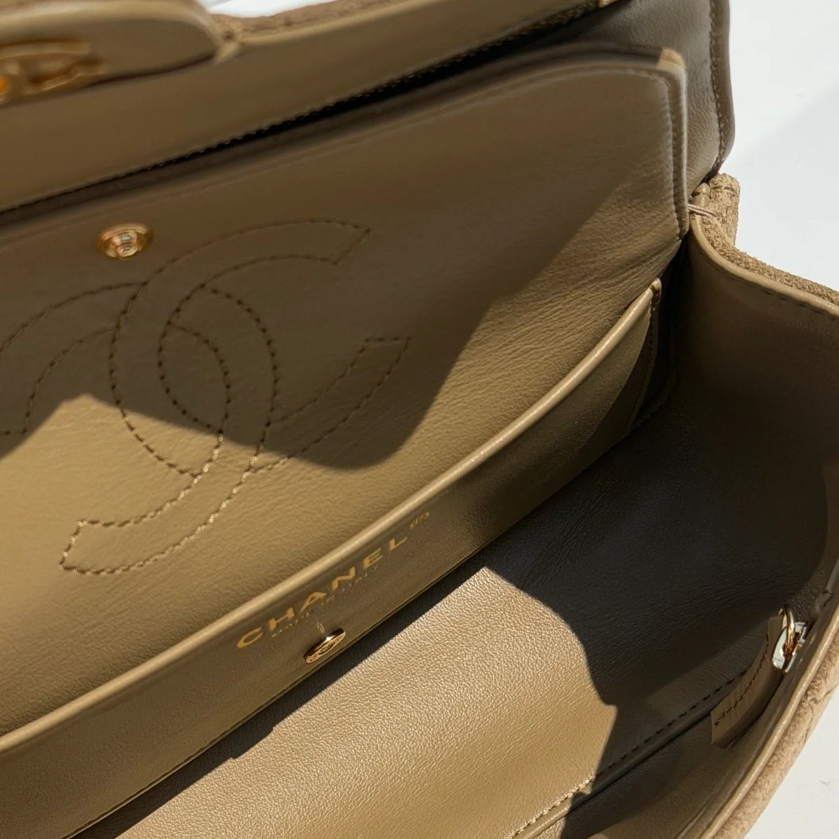 Interior of a beige Chanel leather handbag featuring embossed interlocking CC logo. curated Pre-loved Luxury by Myluxe in Helsinki.