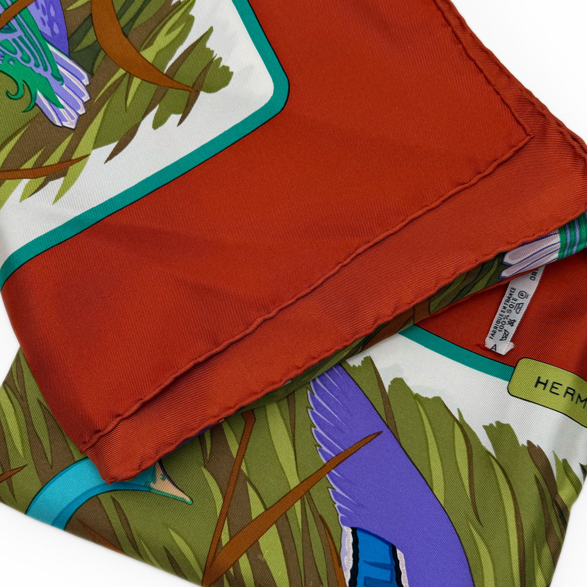 Close-up of a red silk Hermès scarf with colorful bird and nature print, curated Pre-loved Luxury by Myluxe in Helsinki.