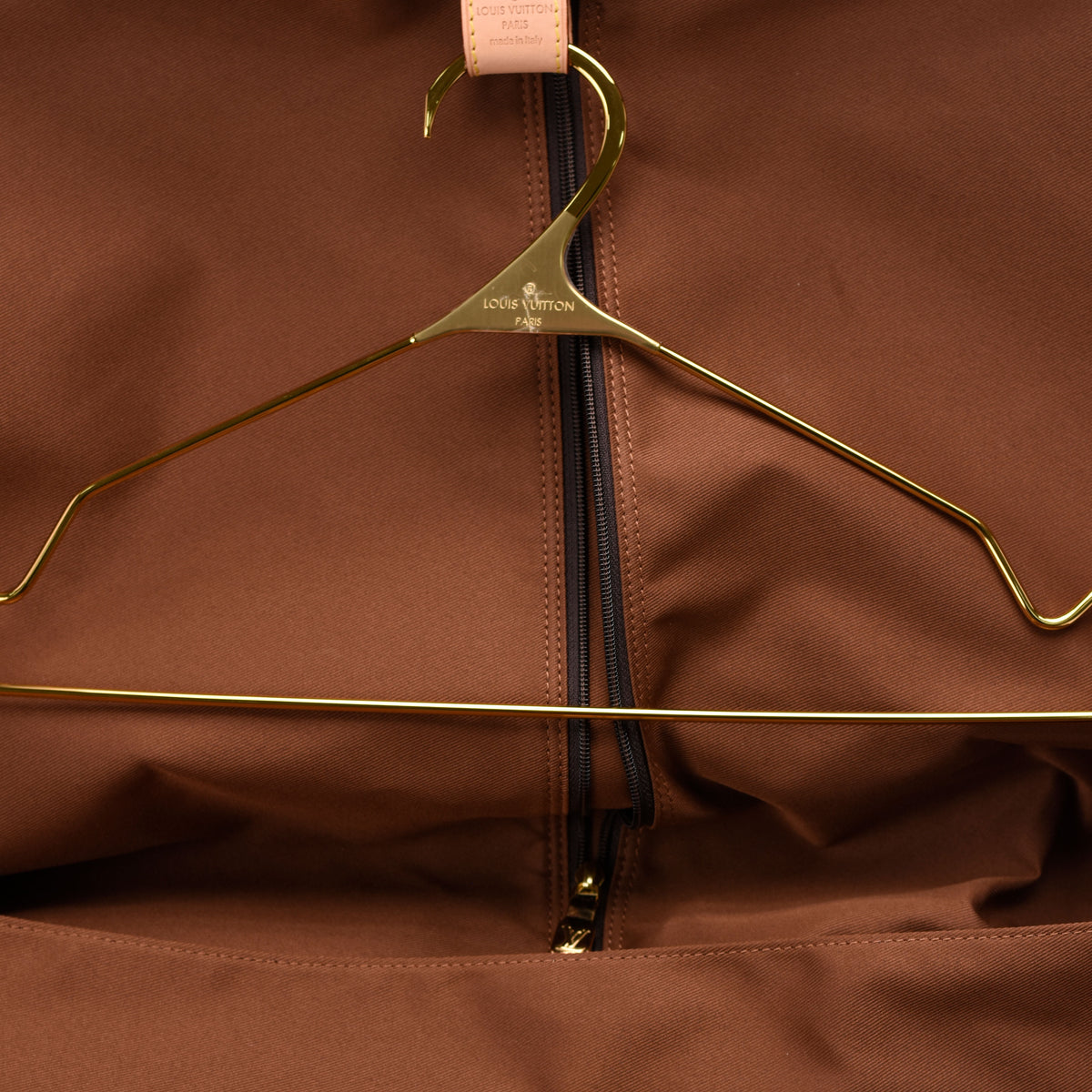 Gold Louis Vuitton hanger inside a brown garment bag, curated Pre-loved Luxury by Myluxe in Helsinki.