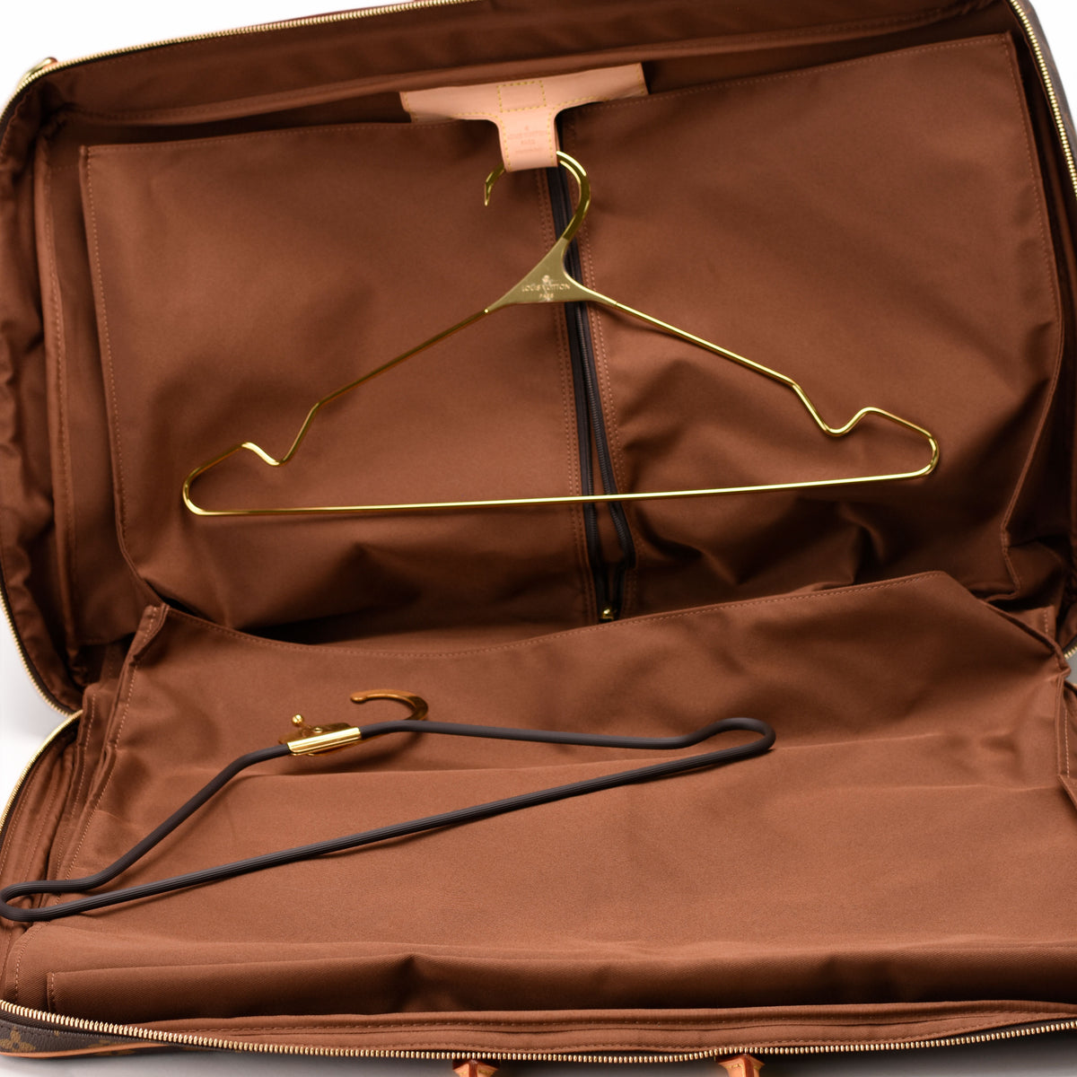 Open brown garment bag with gold and black hangers, curated Pre-loved Luxury by Myluxe in Helsinki.