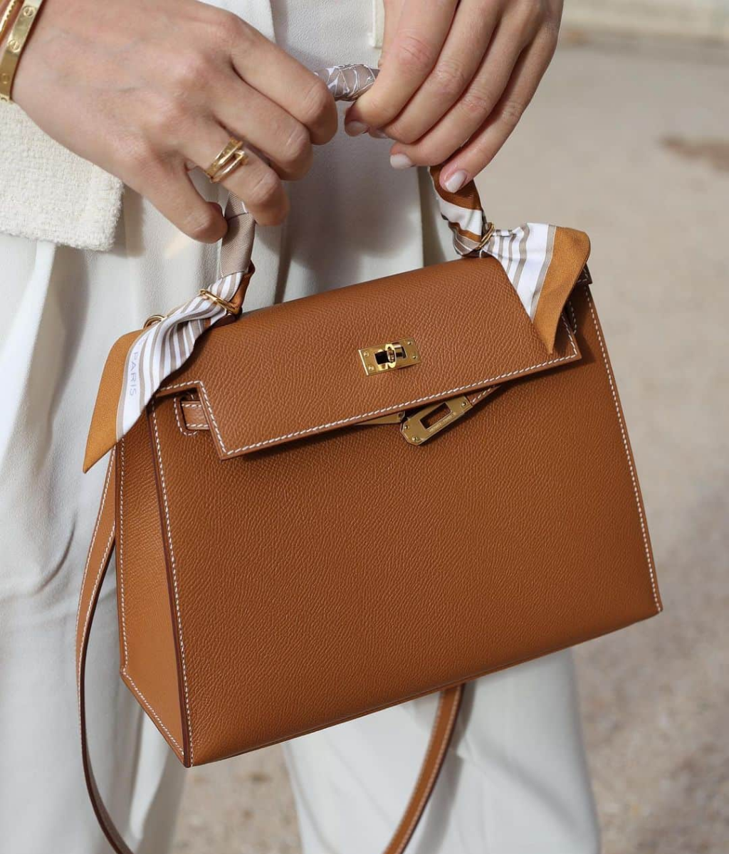 Tan pebbled leather designer handbag with gold hardware and a silk scarf handle wrap.