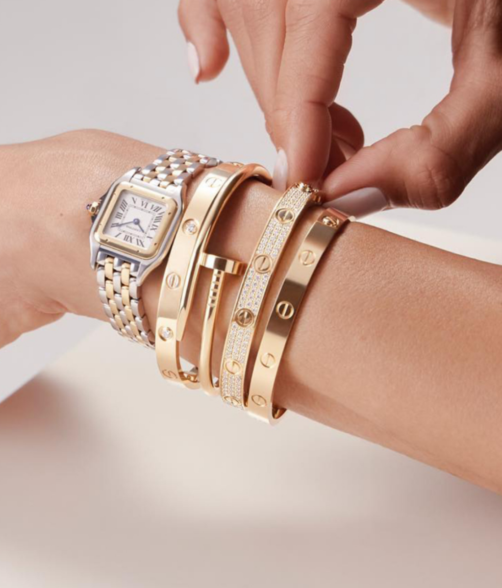 A woman wearing a gold and silver luxury wristwatch paired with several gold designer bangles.