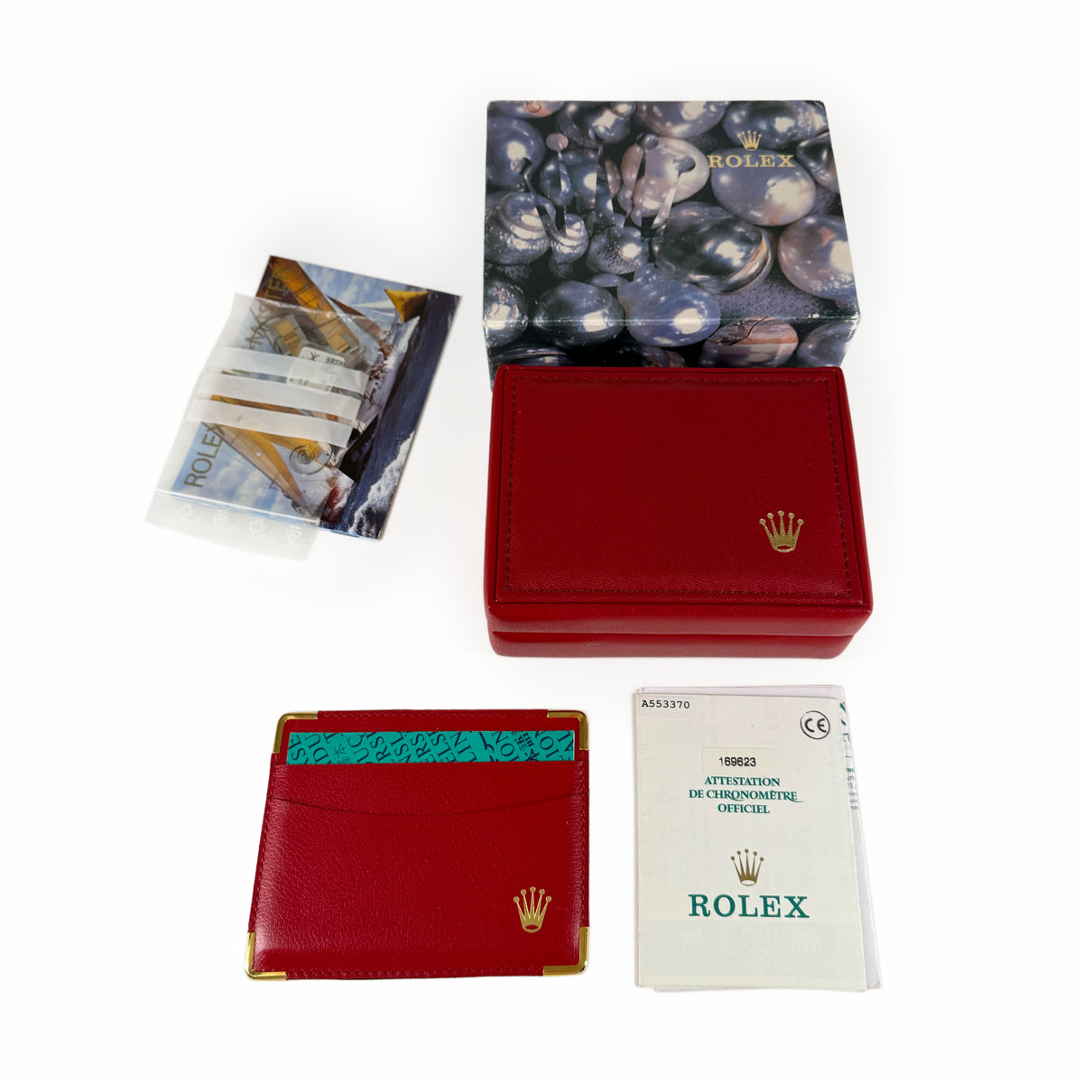 Red leather Rolex accessories including a watch box, card holder, and official certificate, curated Pre-loved Luxury by Myluxe in Helsinki.