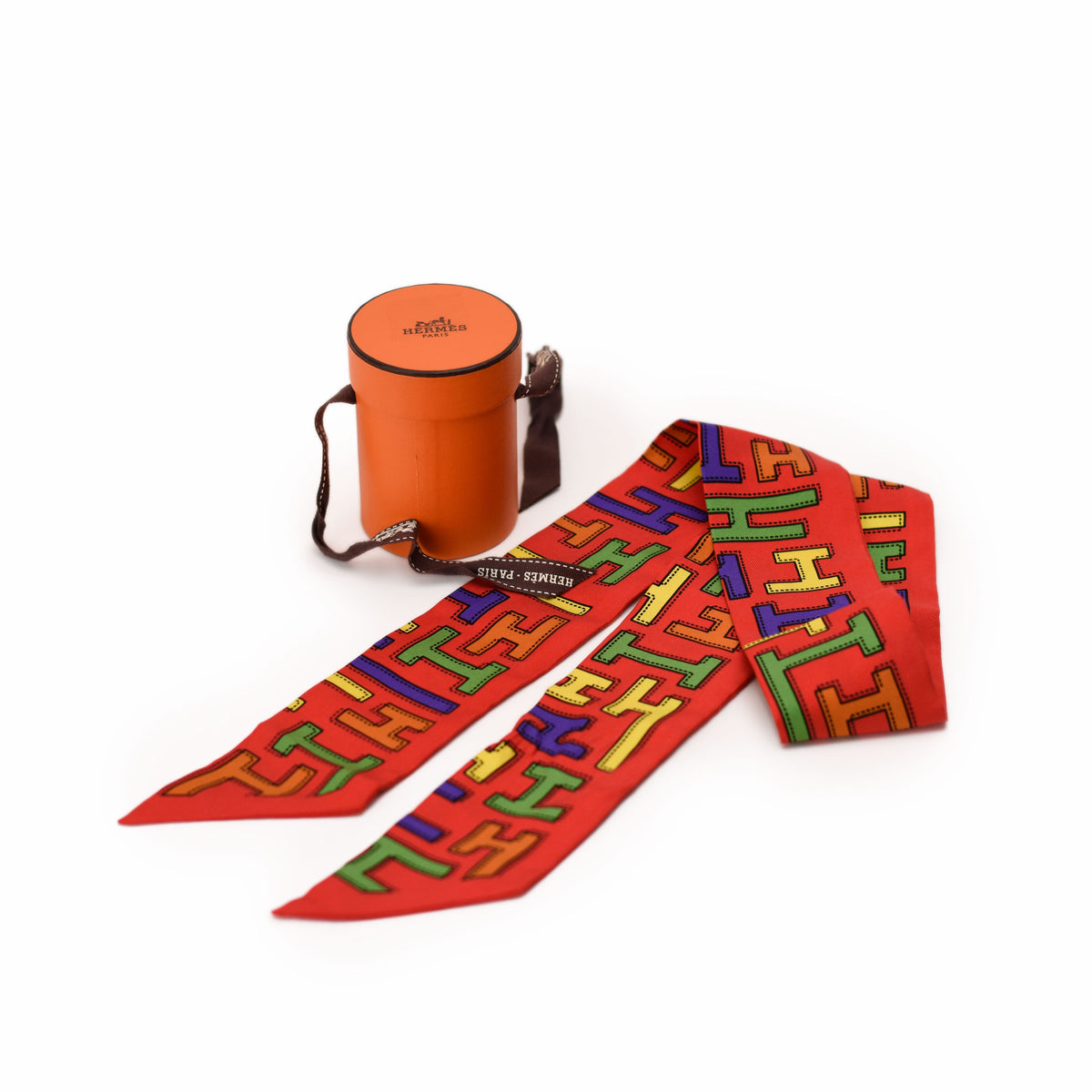 Red silk Hermès twilly scarf with colorful geometric pattern and orange case. curated Pre-loved Luxury by Myluxe in Helsinki.